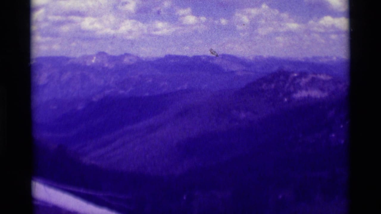 Distant mountain range and valley slopes with cloudy sky and dark film borders.
