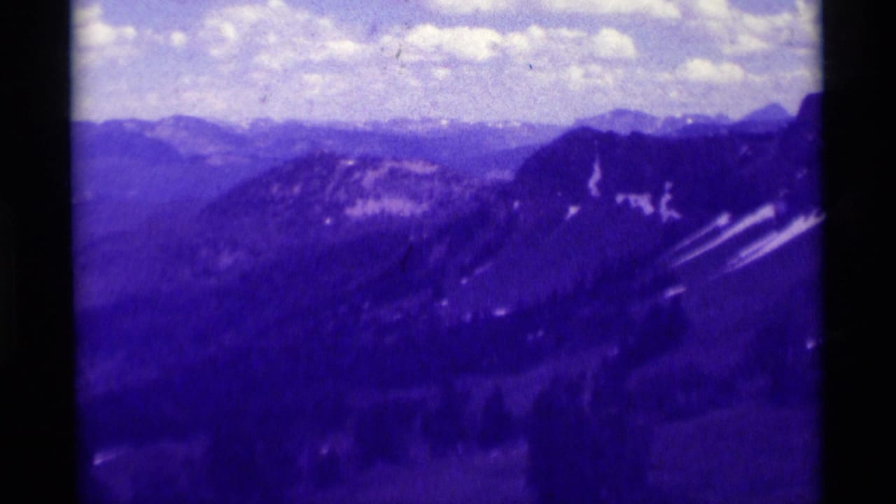 1975 8mm view of distant mountain ranges in Montana, tinted purple with clouds over layered ridges.