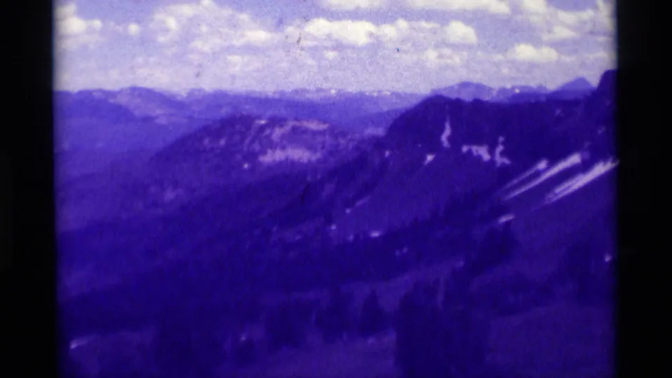 1975 8mm view of distant mountain ranges in Montana, tinted purple with clouds over layered ridges.