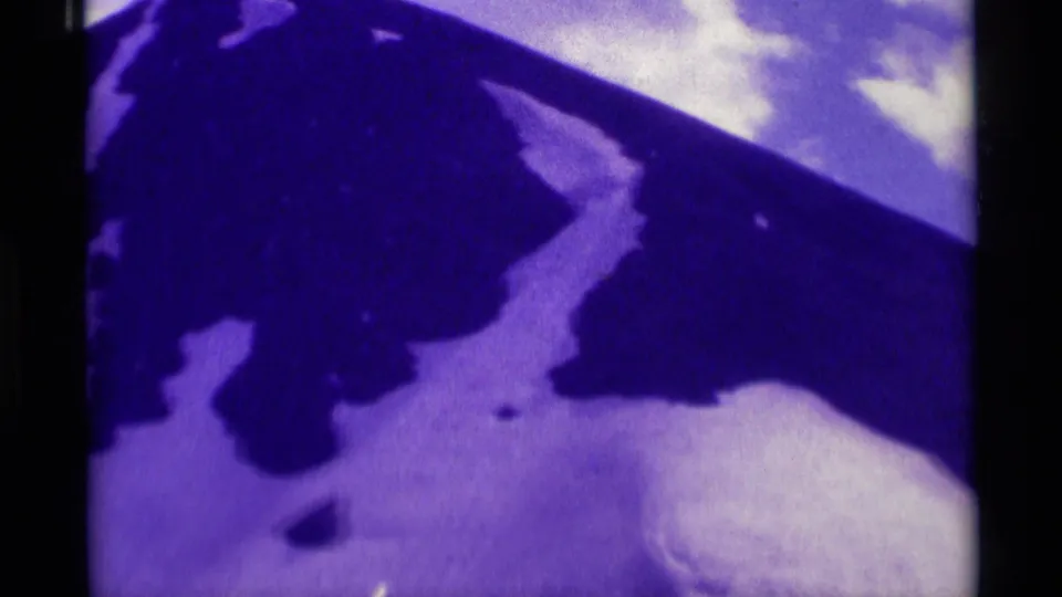 1975 8mm Montana mountain slope showing broad snowfields, dark terrain, and soft purple color shift.