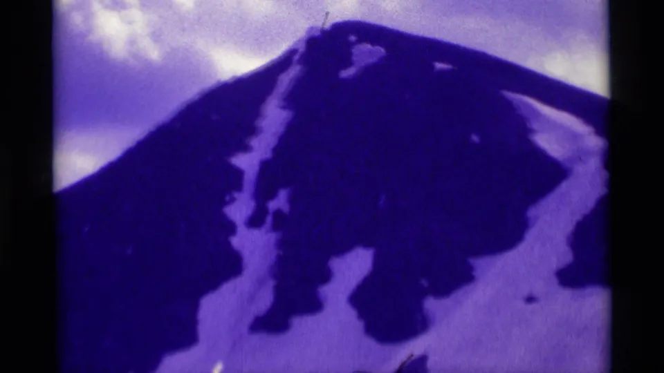 Purple-blue 1975 8mm view of a Montana peak with scattered snow patches and soft home-movie focus.