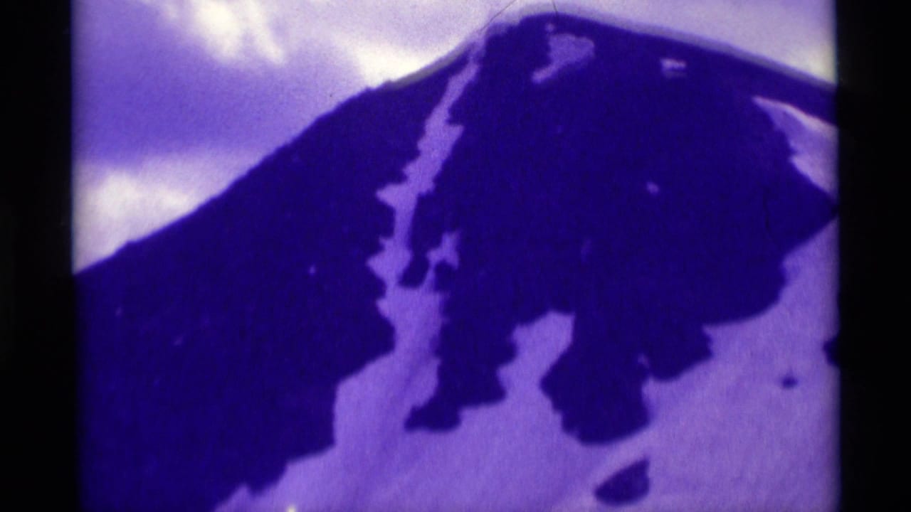 1975 8mm home-movie frame from Agate Springs, Montana showing a dark mountain slope, snow patches, and cloudy sky.