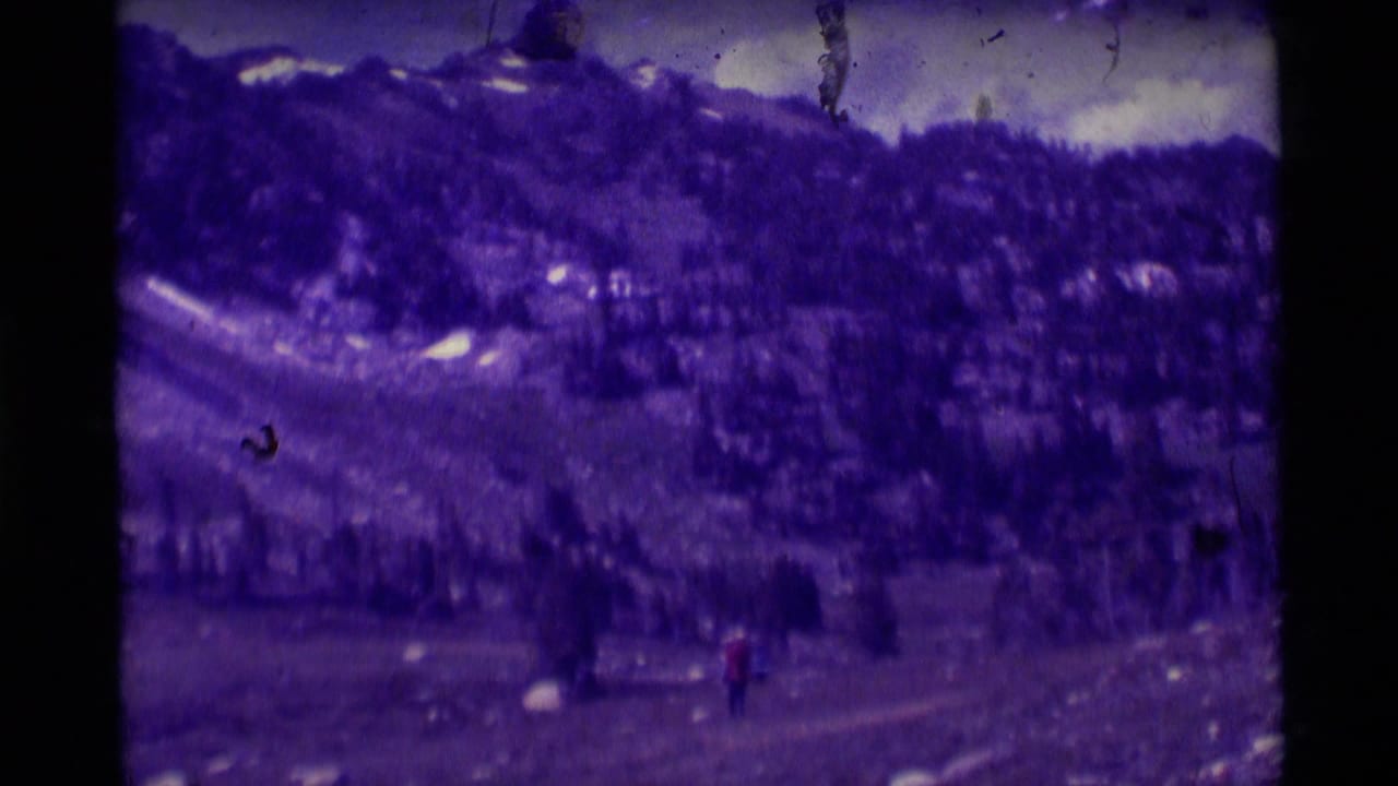 1975 8mm Montana footage shows a distant hiker in red walking through a rocky mountain landscape with evergreen slopes.