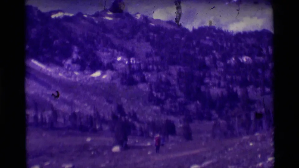 1975 8mm Montana footage shows a distant hiker in red walking through a rocky mountain landscape with evergreen slopes.