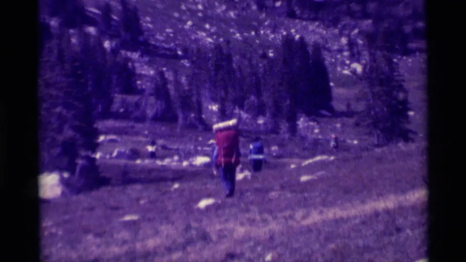 The clip ends with the red-jacketed hiker walking away across rocky Montana mountain terrain in aged 8mm home-movie color.