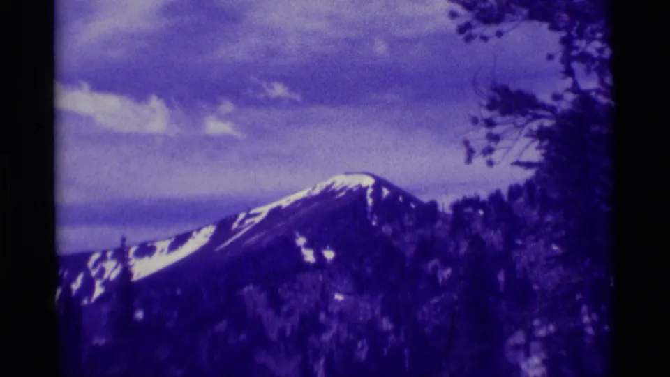 1975 Agate Springs, Montana 8mm frame showing a closer snow-lined mountain slope, forested foreground, and pronounced purple film fading.