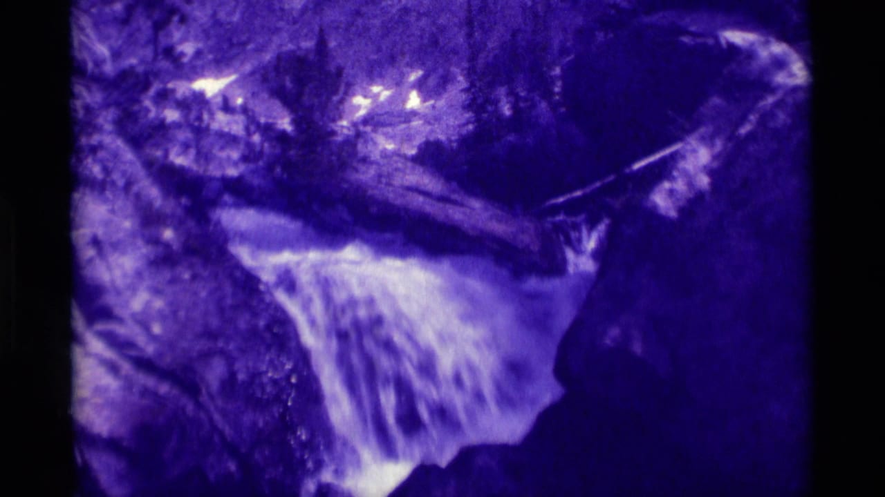 Purple-faded 8mm frame from Agate Springs, Montana, with white water spilling between large rocks and trees in the background.