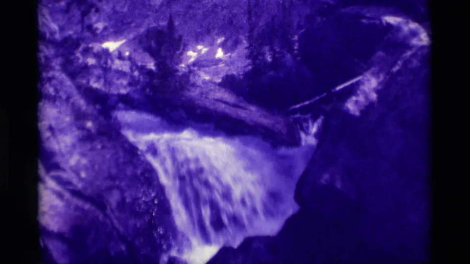 Purple-faded 8mm frame from Agate Springs, Montana, with white water spilling between large rocks and trees in the background.