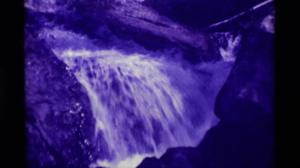 1975 home-movie frame from Montana showing a closer view of foaming waterfall water spreading over dark rock surfaces.
