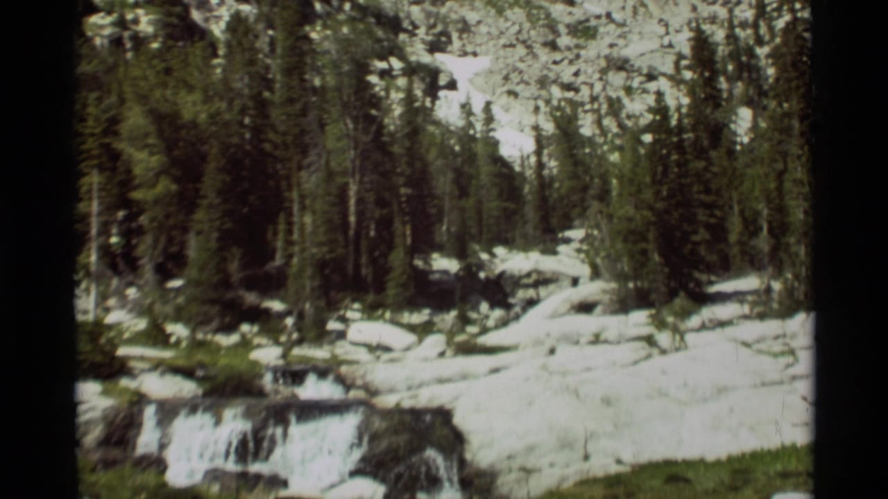 Small cascade in a forest clearing with snow patches and rocks.