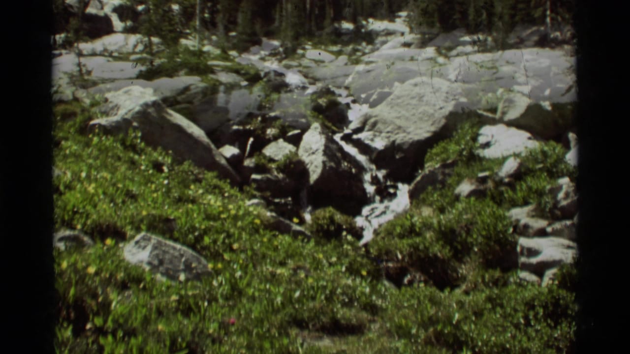 Rocky mountain meltwater channel in Agate Springs, Montana, with snow patches, large stones, and green spring vegetation on 8mm film.