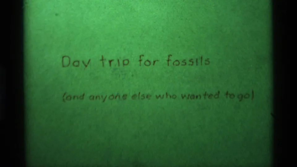 Soft 8mm frame of the Agate Springs fossil day-trip title card, with handwritten brown lettering on green paper.