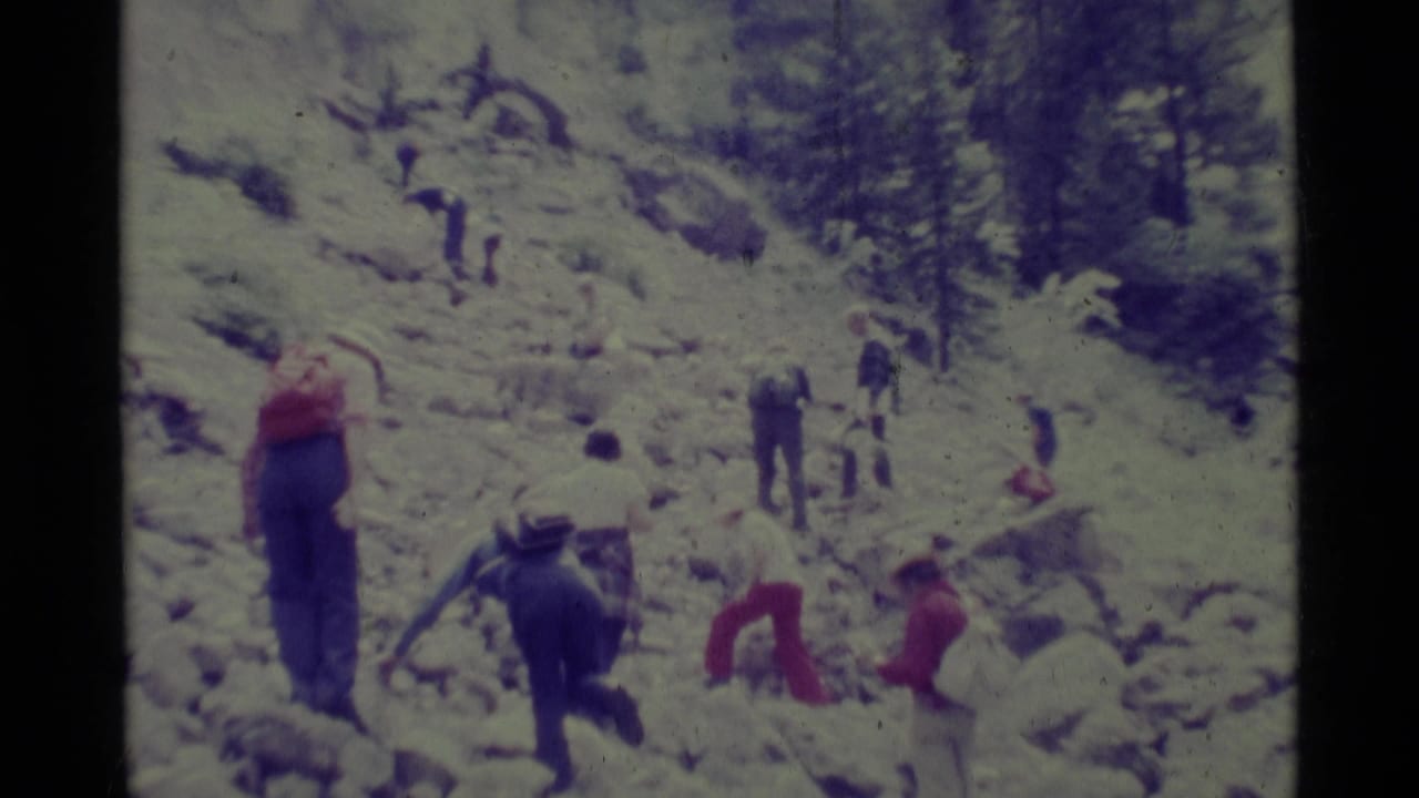 A 1975 8mm home-movie frame shows people hiking across a rocky slope in Agate Springs, Montana.