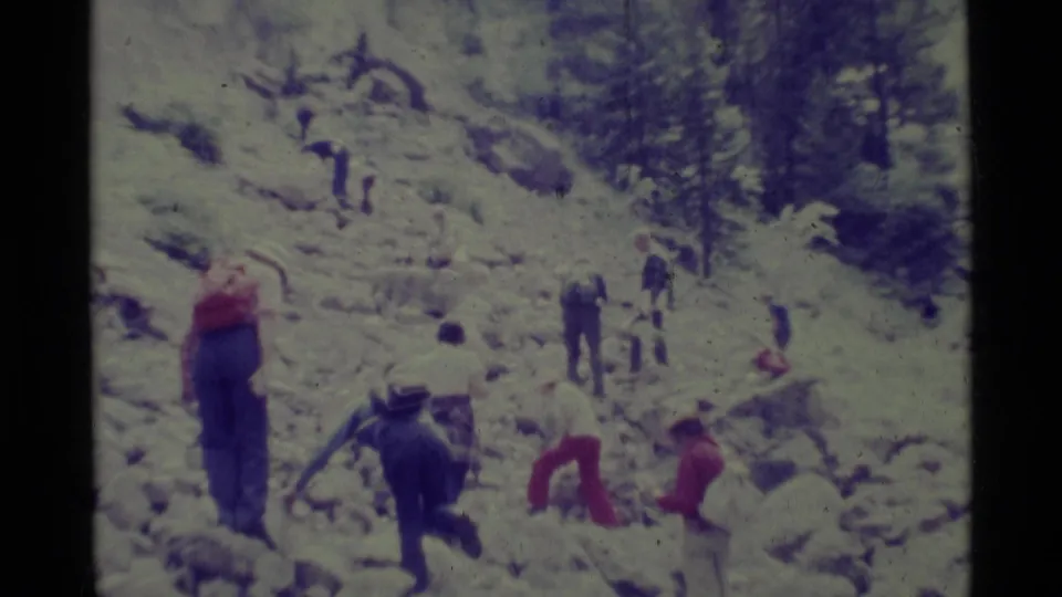 A 1975 8mm home-movie frame shows people hiking across a rocky slope in Agate Springs, Montana.