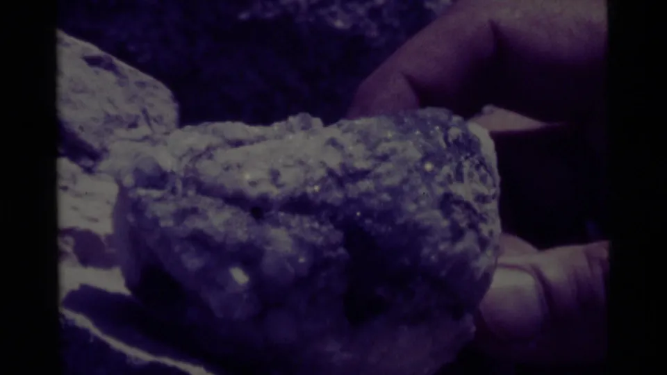 Close-up 8mm view of hands holding a rough mineral or rock specimen during the Montana outing.