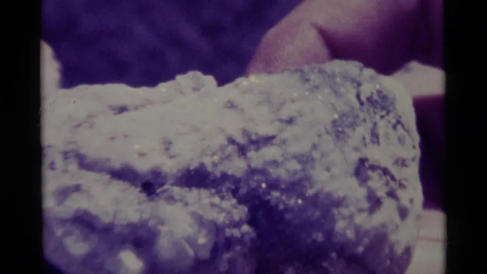 Close-up of a textured rock specimen held near the camera, with a person partially visible behind it.