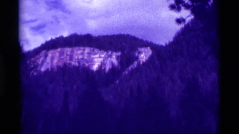 Agate Springs 8mm frame with a rocky hillside, dark forested slope, cloudy sky, and visible film border.