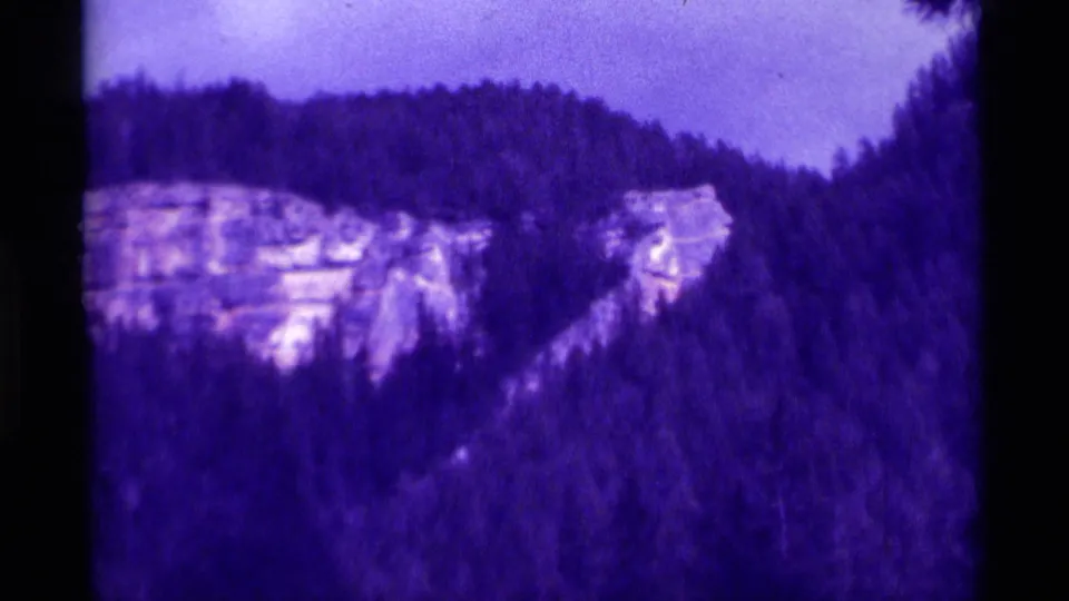 A purple-shifted 1975 8mm view of a wooded Montana ridge with pale exposed rock on the mountainside.