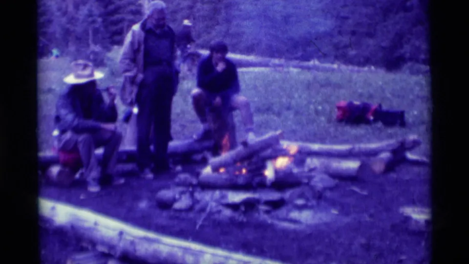 1975 8mm footage from Agate Springs, Montana, shows campers gathered around a small fire in a grassy wooded area.