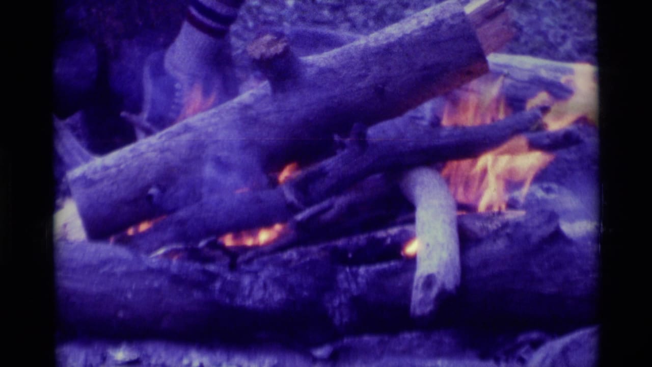 Close view of logs and flames, with smoke drifting across the fire.