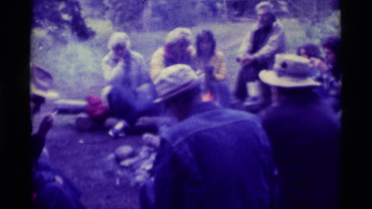 1975 Agate Springs, Montana frame with adults gathered around a campfire, filmed from behind two seated figures in hats.