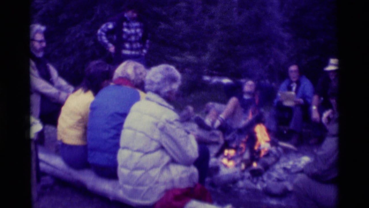 1975 8mm home-movie frame from Agate Springs, Montana, showing a group seated around a campfire in the woods.
