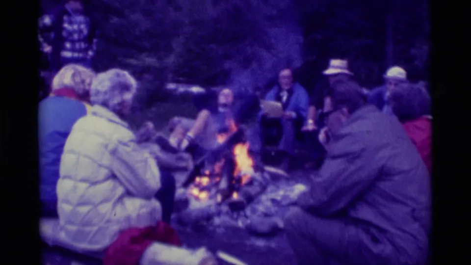 Agate Springs, Montana campfire scene with adults in jackets and hats seated around the flames in a wooded area.