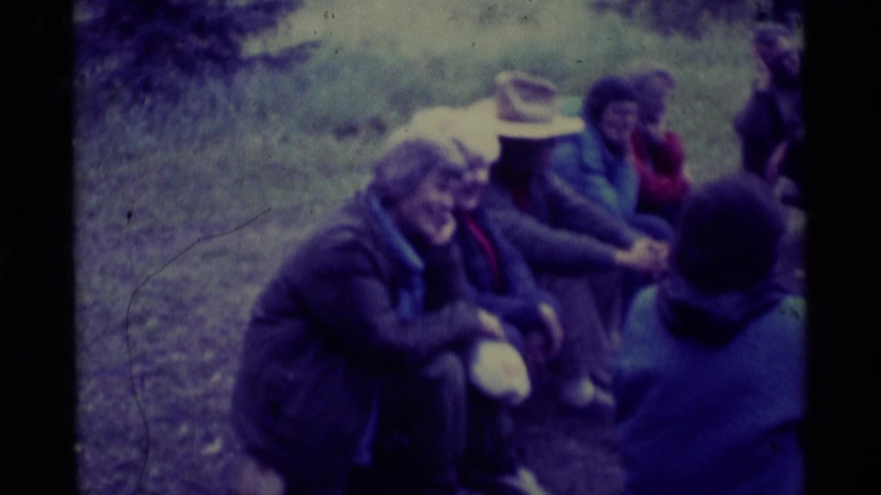 Adults in jackets sit outdoors in a loose circle on grass.
