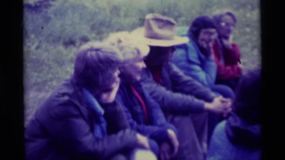 The frame shows a casual 1975 outdoor rest scene with adults seated in a circle-like arrangement at Agate Springs, Montana.