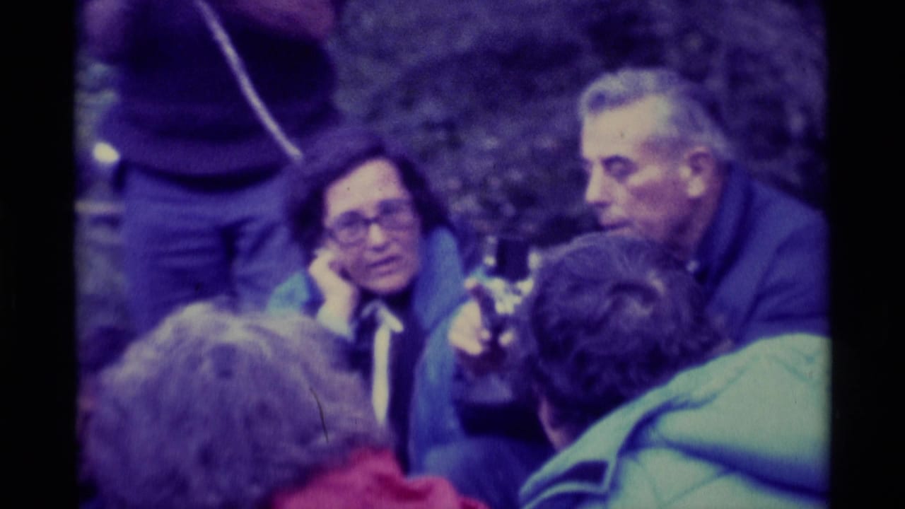 Group seated outdoors around a camera, with two faces visible in the center.