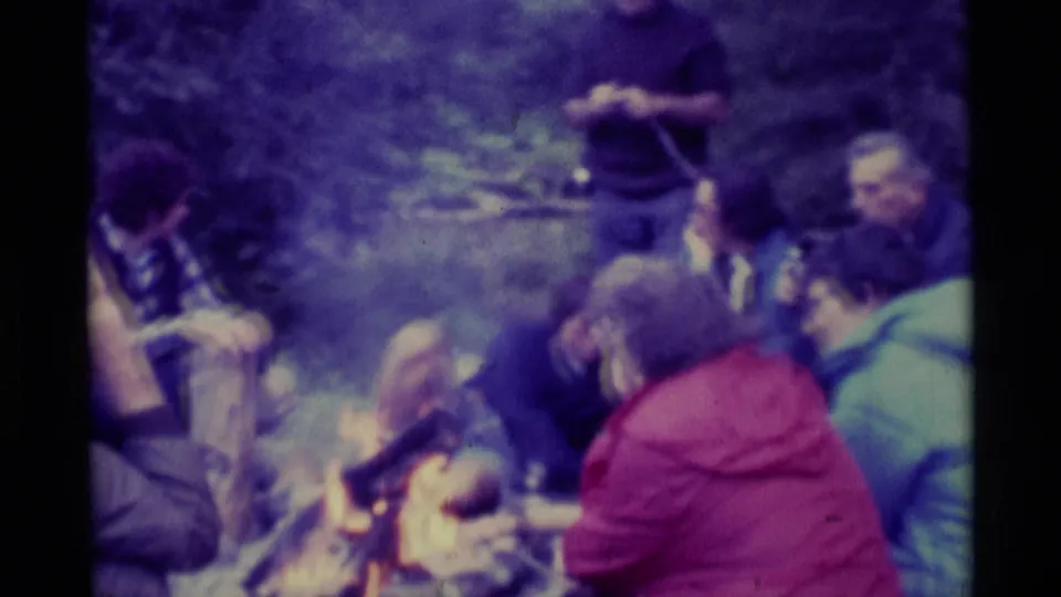 1975 Agate Springs, Montana 8mm frame with adults sitting and standing around a smoky campfire.