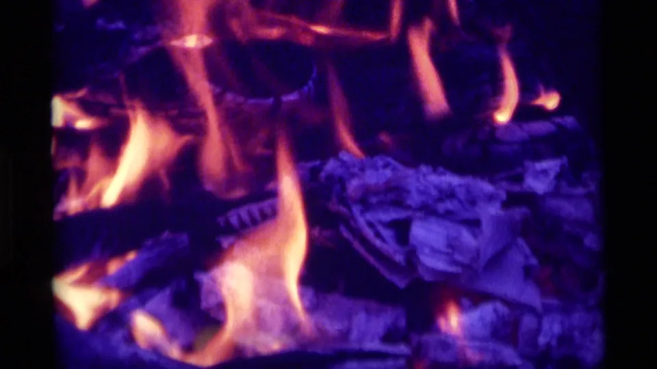 Close home-movie frame of tall flames and stacked logs, with strong purple-orange 8mm color shift.