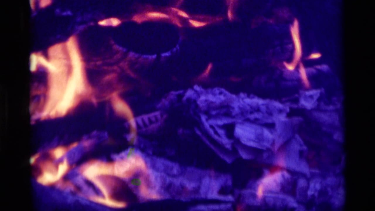 1975 8mm home-movie frame from Agate Springs metadata showing close firelight, embers, and saturated blue-purple color.