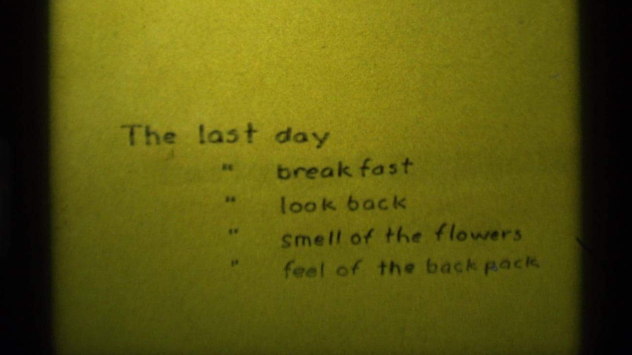 1975 8mm home-movie frame from Agate Springs, Montana showing a handwritten last-day list on yellow paper.