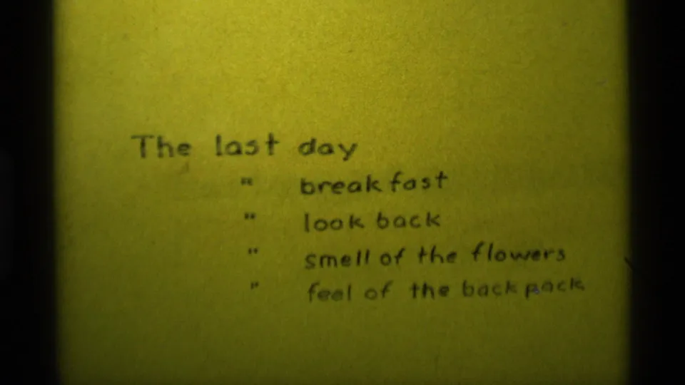 1975 8mm home-movie frame from Agate Springs, Montana showing a handwritten last-day list on yellow paper.