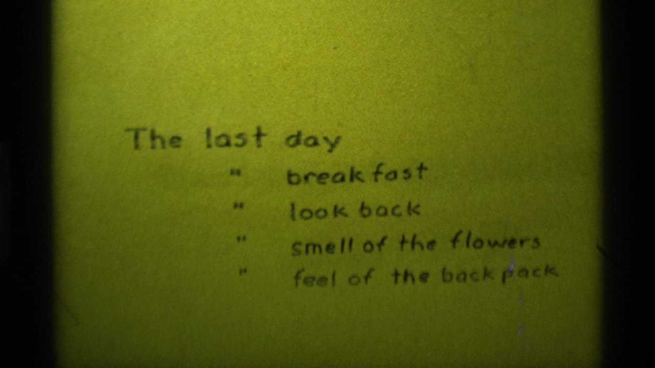 1975 8mm frame from Agate Springs, Montana showing a handwritten final-day memory list on yellow-green tinted film.