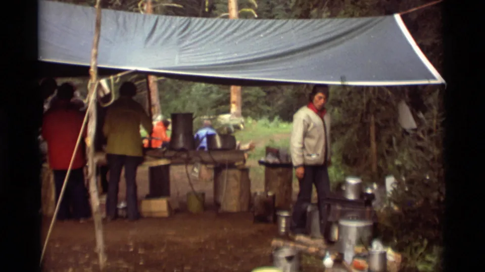 1975 Agate Springs, Montana frame with campers at a forest cooking station, including visible pots, tables, and a tarp canopy.
