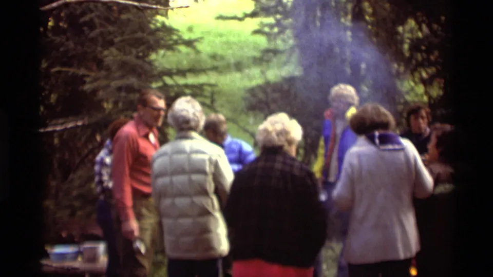 Agate Springs 8mm frame with adults facing a smoky campfire area, surrounded by trees and casual outdoor clothing.