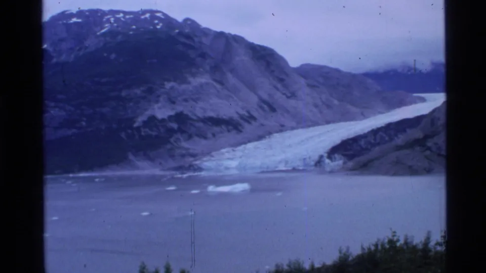 Alaskan glacier and mountain fjord scene on 8mm film, with floating ice and dark scanned frame edges.