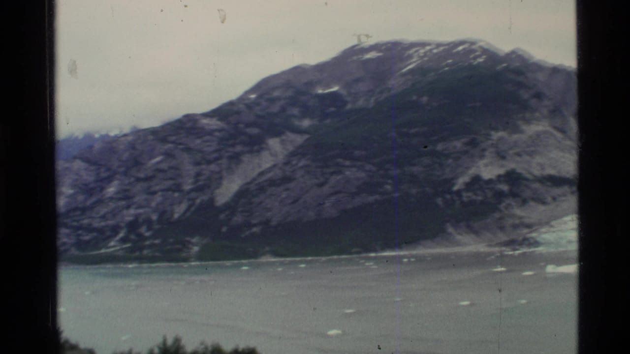 Rocky mountain above a calm fjord with small floating ice pieces.