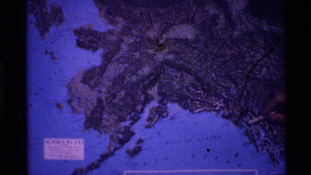 Relief map of Alaska with a hand pointing near the right edge.