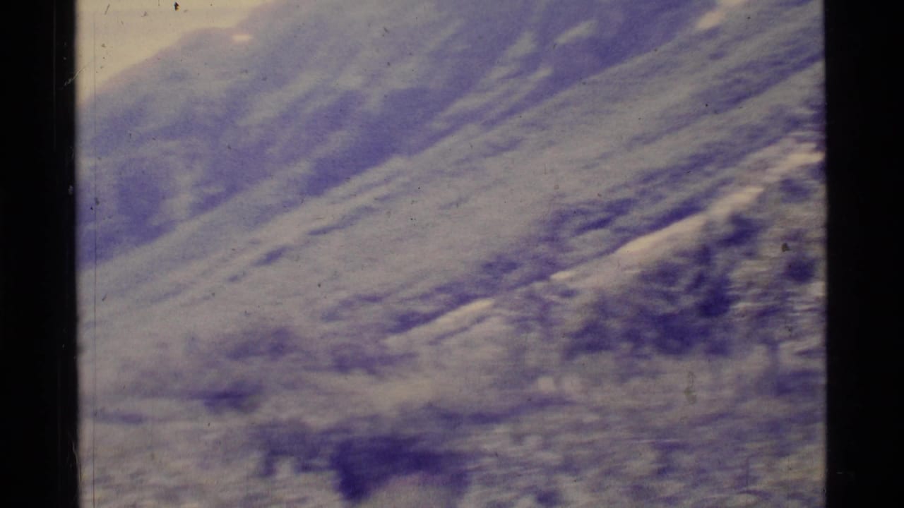 Snow-streaked mountain slopes and a hazy valley seen through dark 8mm film borders.