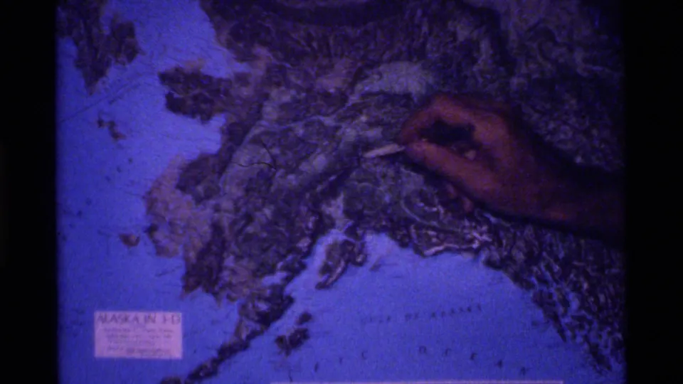 The pointer rests over another region of the Alaska relief map in a grainy 8mm educational shot.