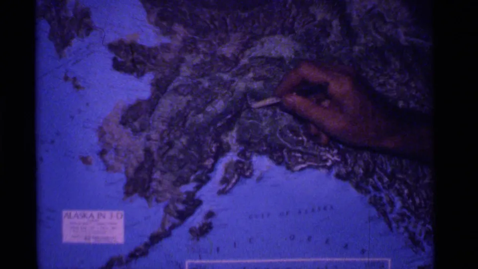 A hand indicates a specific area on the Alaska 3-D relief globe, with coastline and label visible.