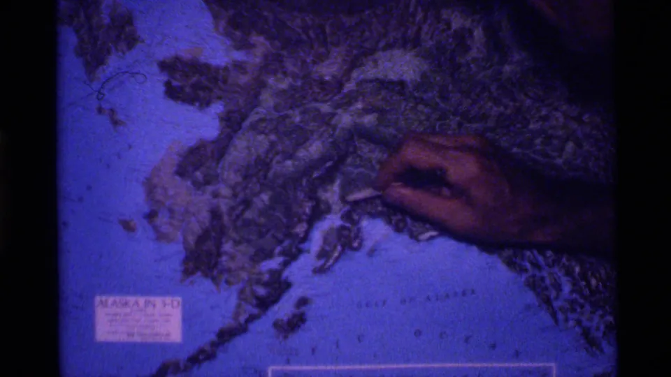 Final frame shows the guide’s hand pointing at raised Alaska terrain on a blue-tinted 3-D globe.