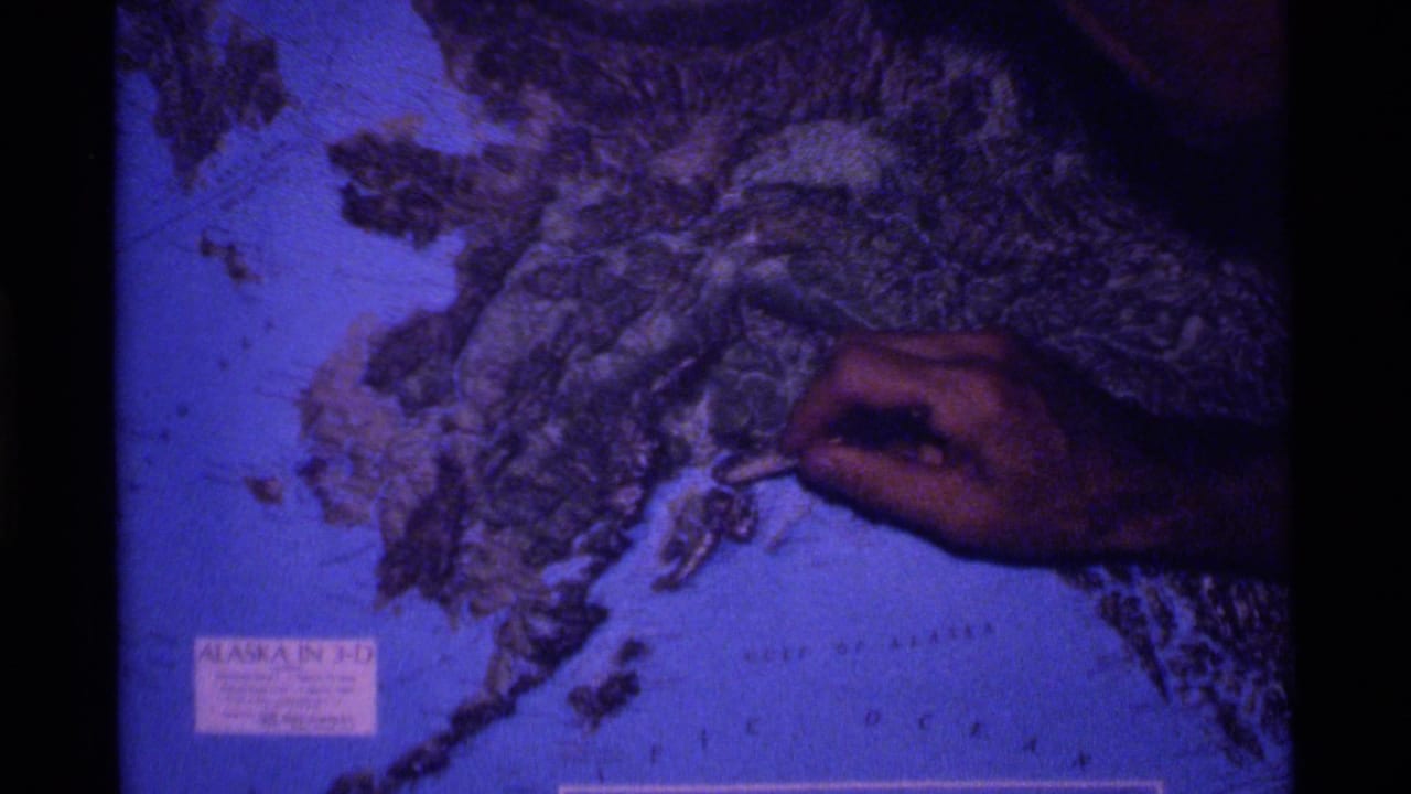 Hand hovers over the lower right area of a relief map of Alaska.