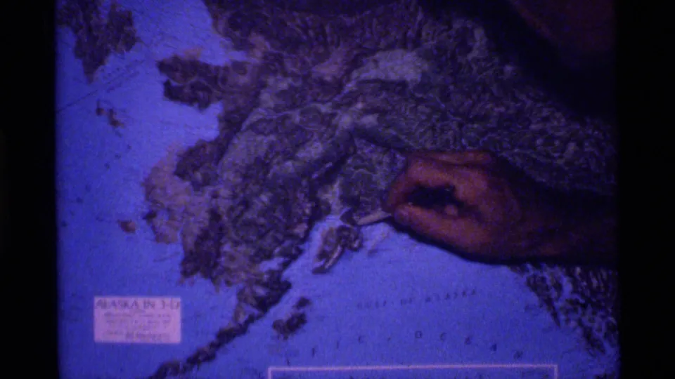 The final frame shows a hand still indicating Alaska's textured terrain on a blue-toned 1977 8mm relief map view.