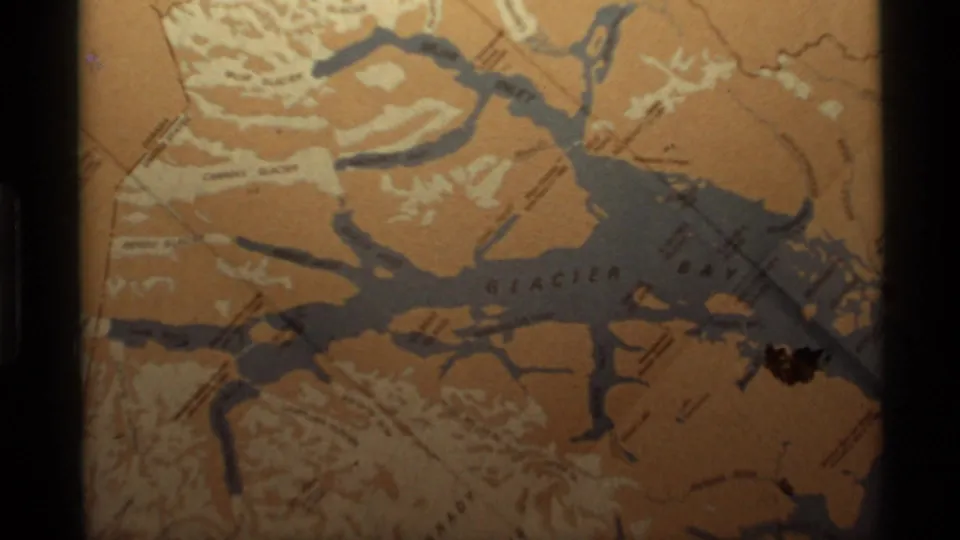 Close 8mm frame of the Glacier Bay map, showing printed labels, gray inlets, orange land, and dark film borders.