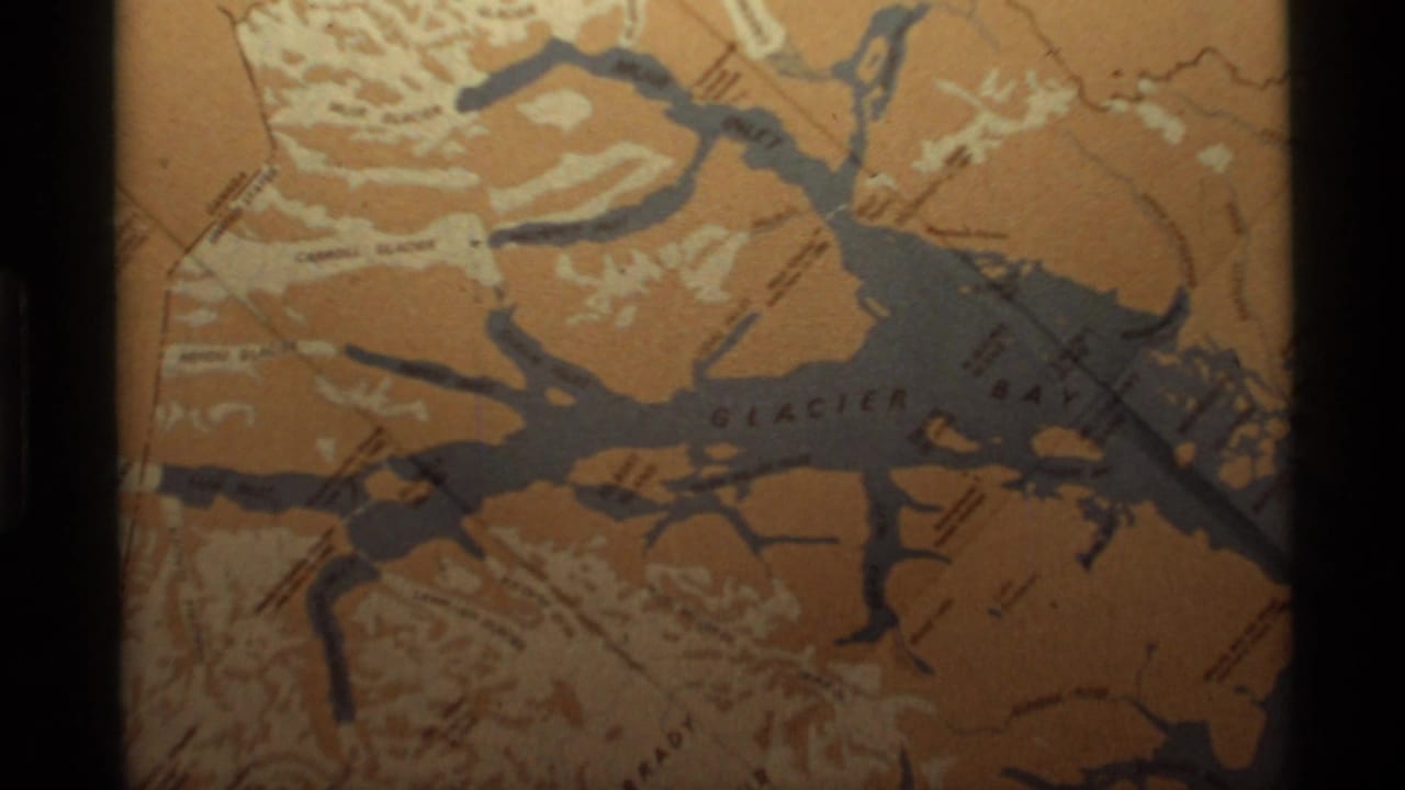 1977 Alaska 8mm frame showing a warm-toned Glacier Bay map panel with blue inlets, white relief marks, and dark film borders.