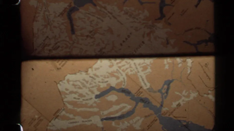 Warm 8mm close-up of an Alaska map section, with blue waterways, pale relief lines, and soft film exposure.
